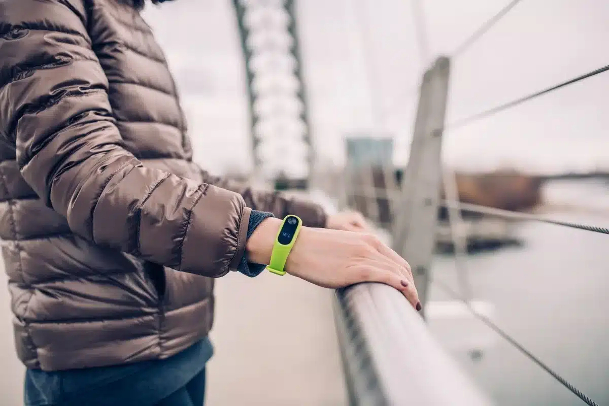 Titanium smartwatch with sapphire crystal display lying on a dark surface, showing the square bezel and side buttons in detail, with water droplets on the screen