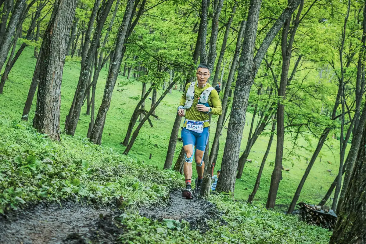Athlete's wrist wearing the watch during outdoor trail running, showing the device in action with a blurred mountain landscape background