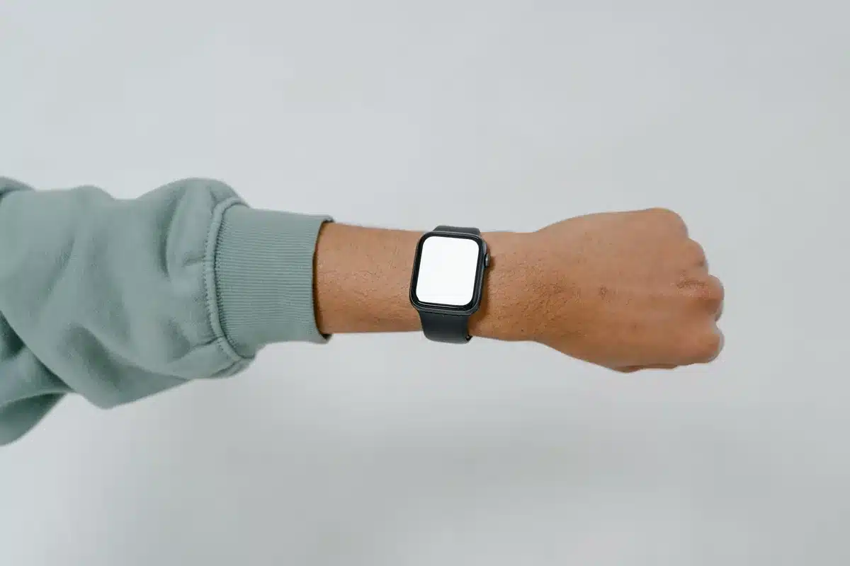 Smartwatch with square AMOLED display showing fitness metrics, titanium bezel catching light, on a wrist during outdoor training, morning sunlight