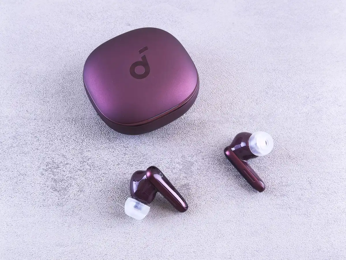 Circular smartwatch display showing music controls and heart rate data, stainless steel bezel gleaming, paired with wireless earbuds on a training surface