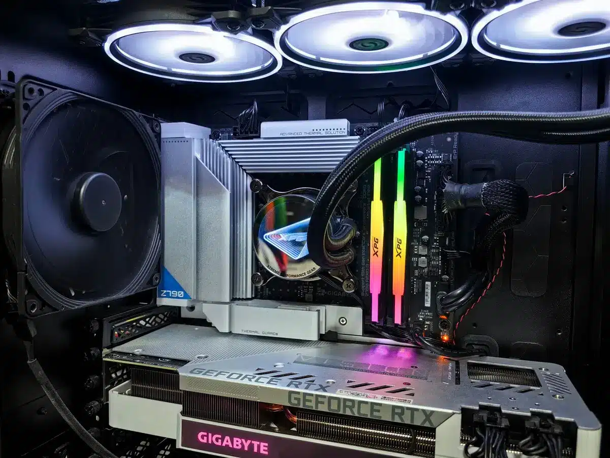 A high-end gaming PC setup with open case showing GPU, CPU cooler, and RAM modules installed, illuminated by RGB lighting against a dark background.