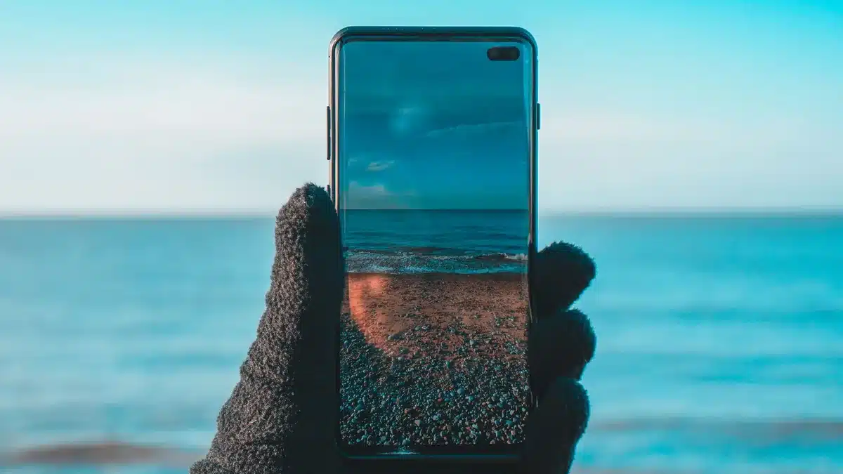 Anonymous hands holding a smartphone displaying vibrant colors on its AMOLED screen in bright daylight, the display catching light with vivid detail.