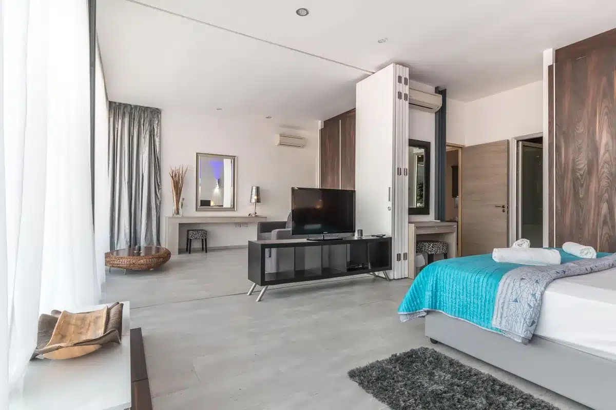 A gray fabric sofa bed in open position showing the flat sleeping surface, positioned in a bright modern living room with natural light from a window, emphasizing the compact space-saving design