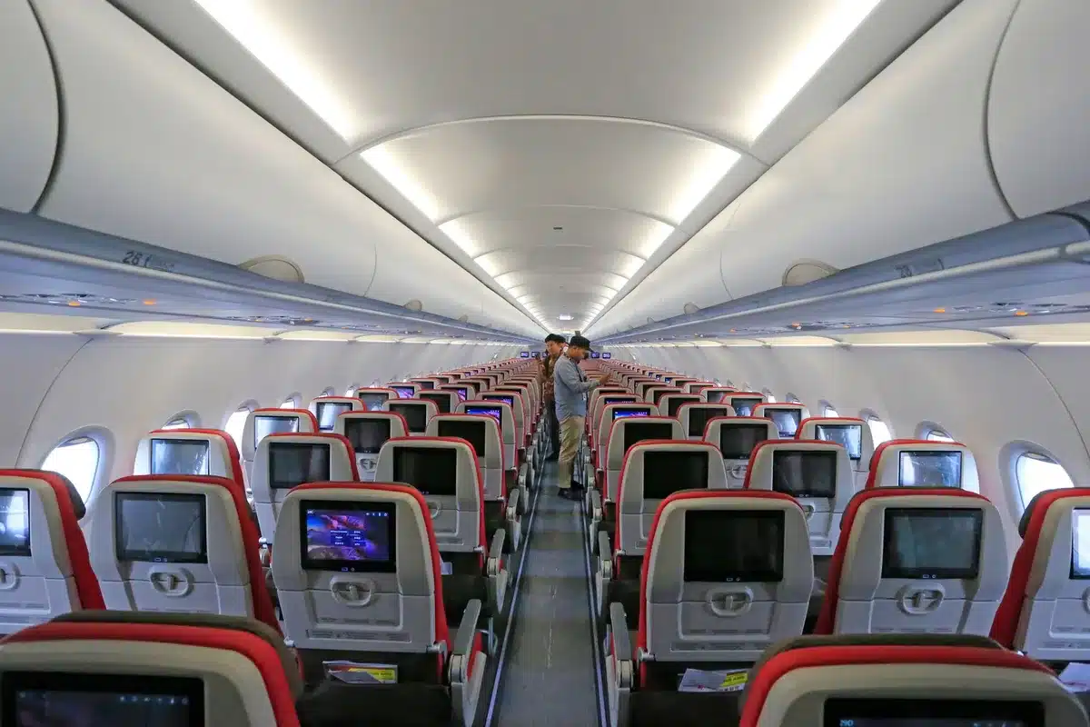 Airplane cabin interior with passengers using devices connected to WiFi, warm cabin lighting reflecting off screens, seamless connectivity enabling work and entertainment at altitude