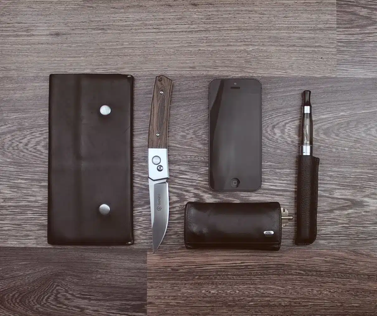 Flat lay of smartphone accessories arranged around device—charging cable, earbuds, protective case—all minimalist design, cool neutral tones, overhead shot