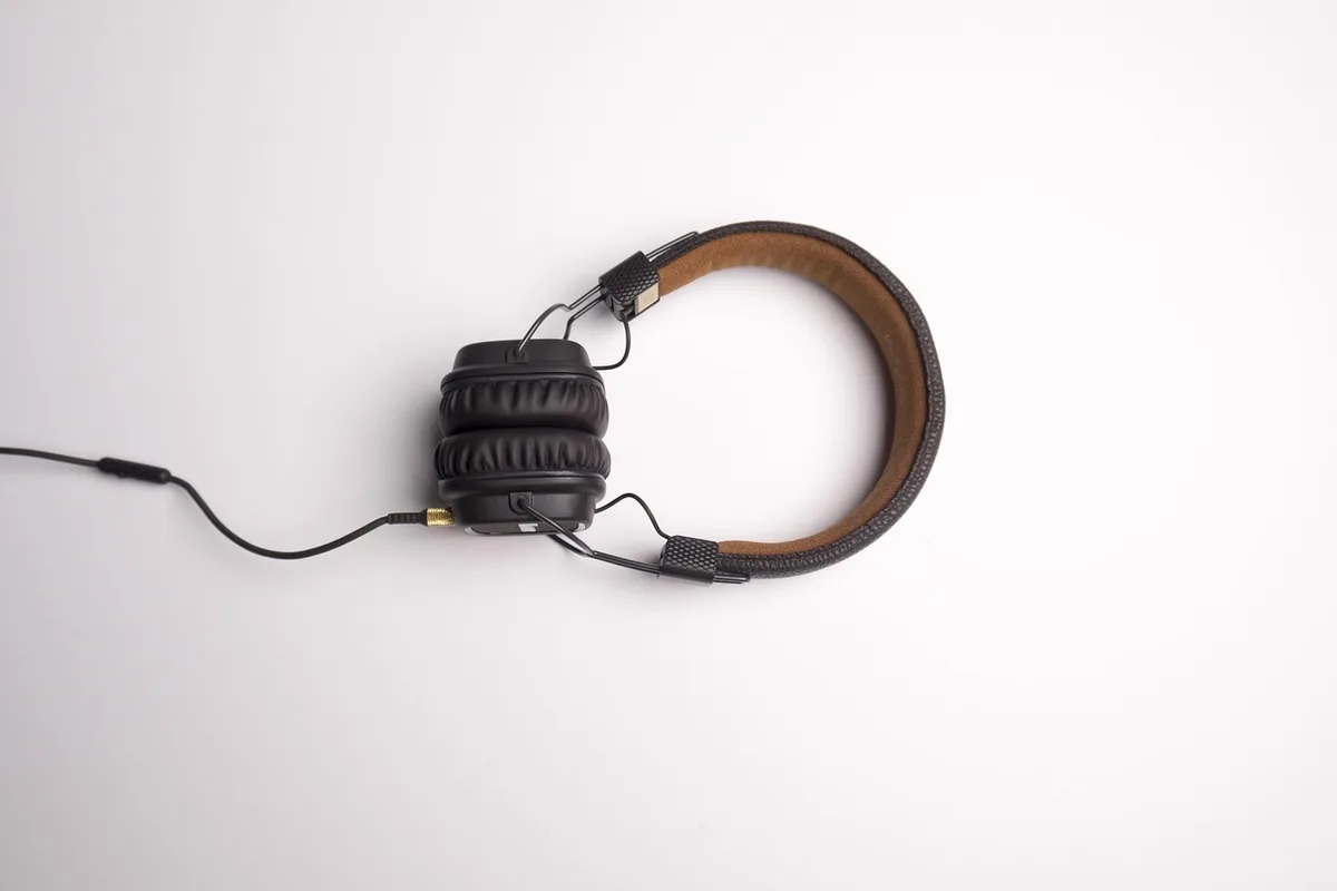 Close-up of fabric ear pad being swapped by anonymous hands next to a charger cable, generic studio table, no brand