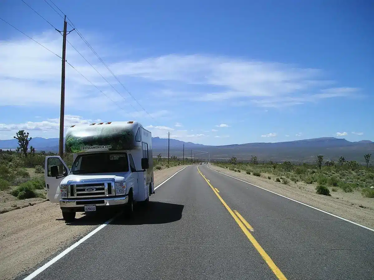Caravana arruinada y silueta anónima en una carretera chamuscada, ambiente tenso