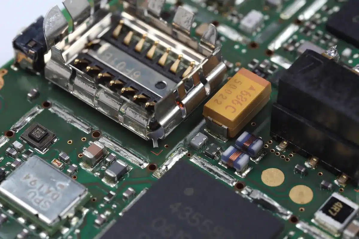 Close-up of anonymous circuit board and loose chips on an anti-static mat, technician hands out of frame, no brand identifiers