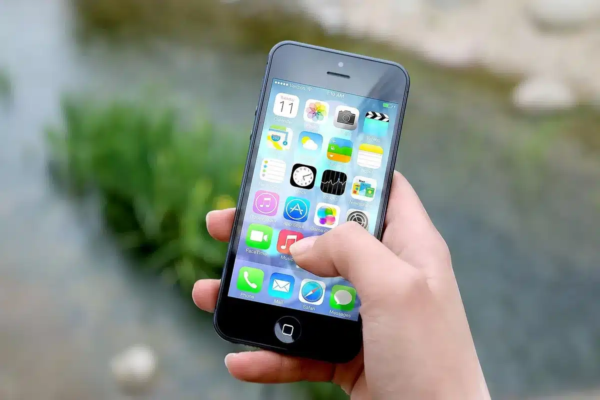 A shopper's hands holding a plain cardboard box with a small anonymous smartphone box visible inside, neutral home table background, sunlight from window