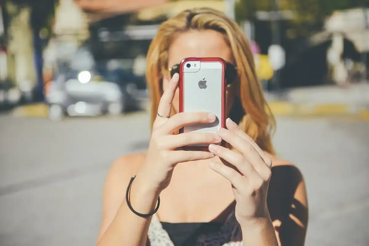 two anonymous hands holding an old mobile phone beside a notepad and magnifying glass, no brand visible