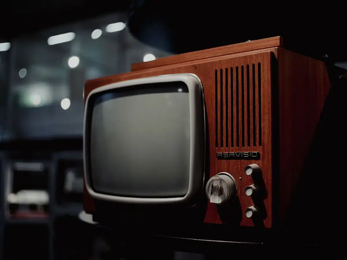 empty vintage television set on a plain wooden table in a living room corner, soft natural window light, a stack of DVDs and a remote beside it