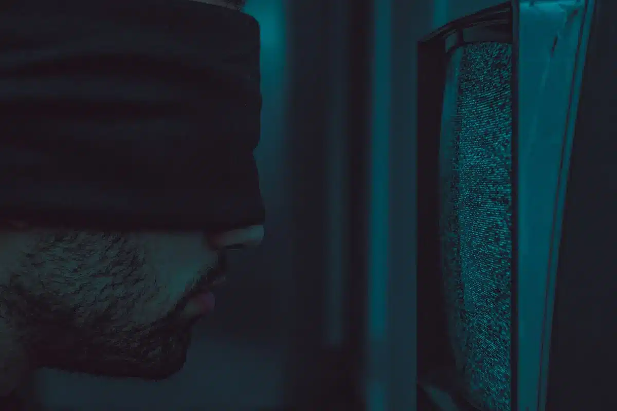 anonymous person watching a TV screen from behind, silhouette on a sofa, warm living room glow, visible remote in hand