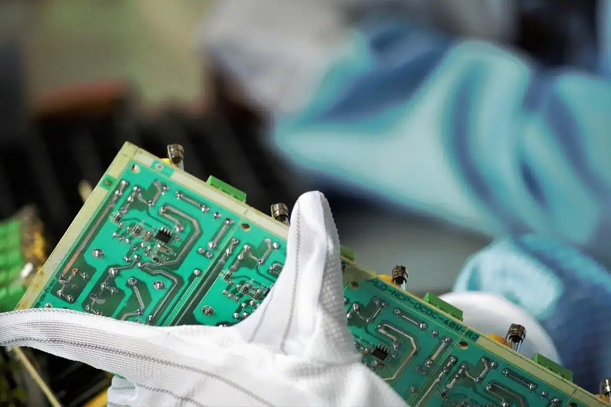 Console manufacturing facility with circuit boards and semiconductor components in harsh industrial lighting, metal workbenches with precision equipment.