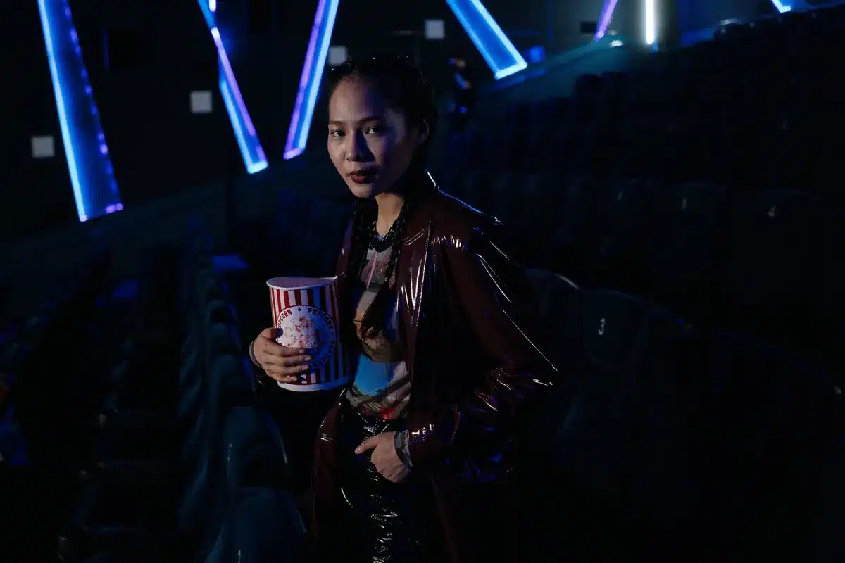 empty theater screen with a single spotlight on stage, an abandoned popcorn tub in a seat, soft grainy film texture
