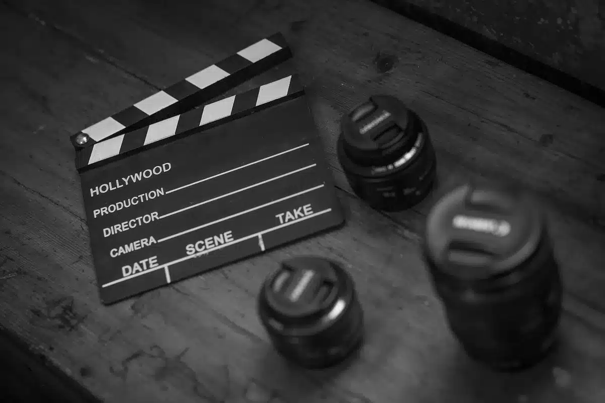 close-up of a torn film strip and a clapperboard resting on a dark table, faint studio lights in background