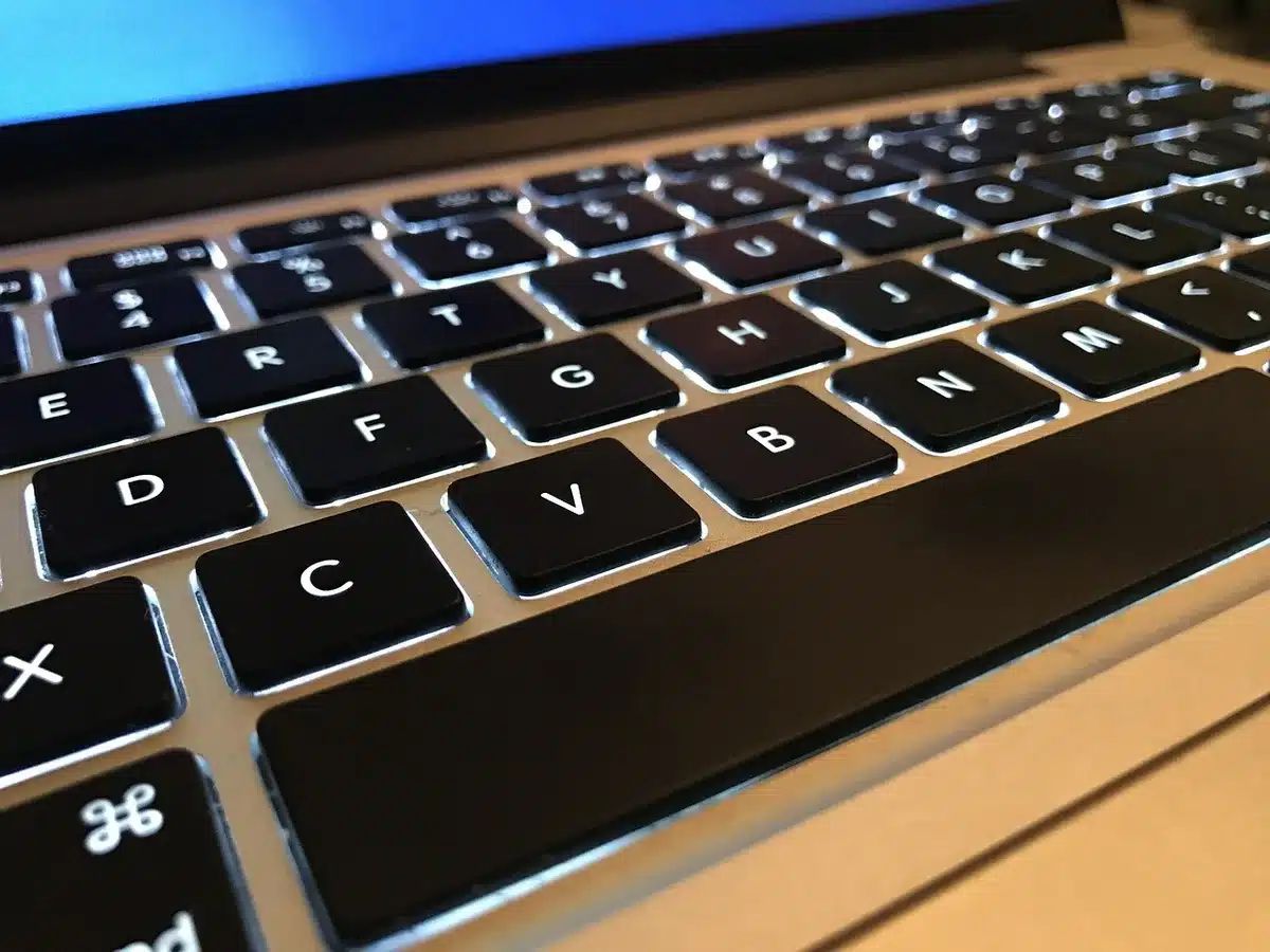 Close-up of anonymous hands hovering over a Mac keyboard in soft light, screen blurred with a permissions dialog out of focus