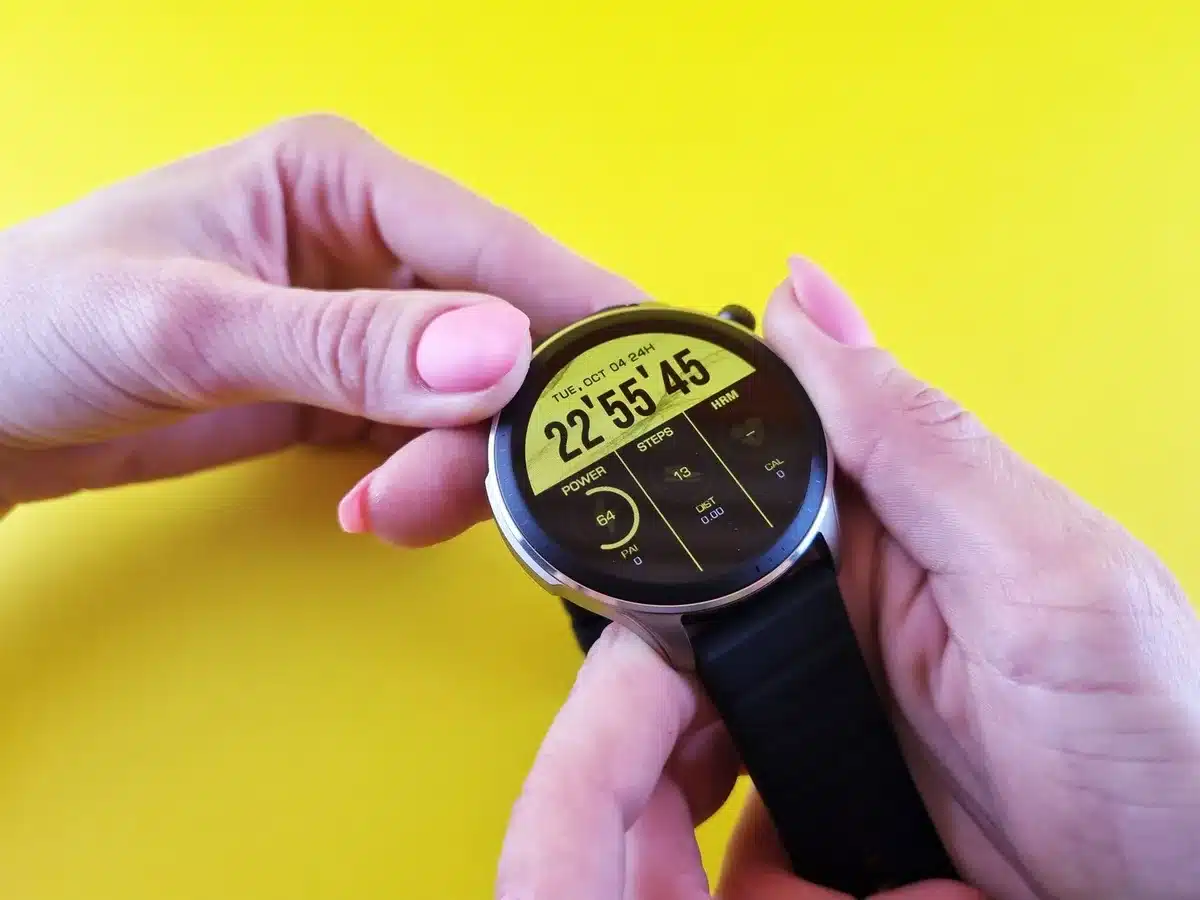 A close-up of an anonymous smartwatch face displaying abstract circular indicators and a readiness score, on a wooden table beside a coffee cup