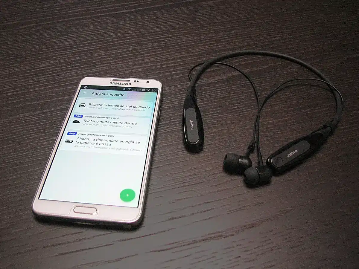 Close-up of an anonymous smartphone lying beside a pair of unbranded earbuds and a generic charging cable on a wooden table; no logos or identifiable packaging