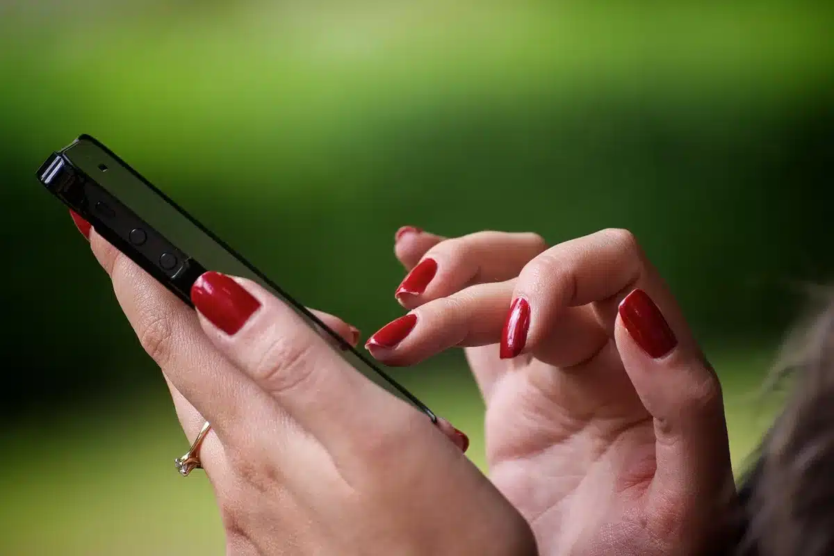 A close-up of an anonymous pair of hands swiping through a photo gallery on a generic phone, the screen showing before-and-after cleanup of a beach scene