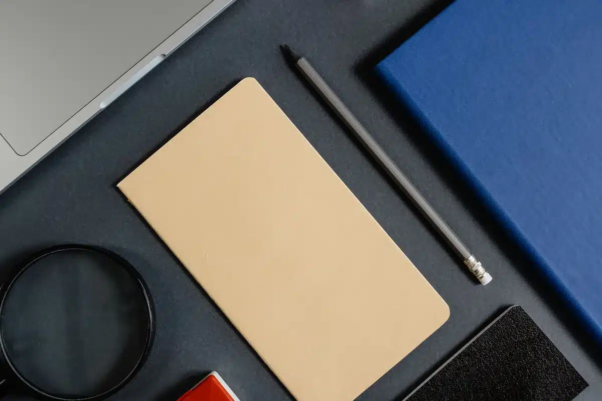 Close-up of an anonymous hand holding an open notebook with technical notes and a small schematic of a foldable phone drawn, coffee cup in background, soft indoor light