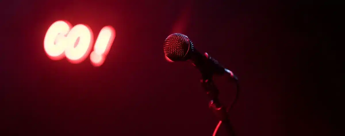 Empty party stage with a single microphone stand under a spotlight, scattered confetti on the floor, no people