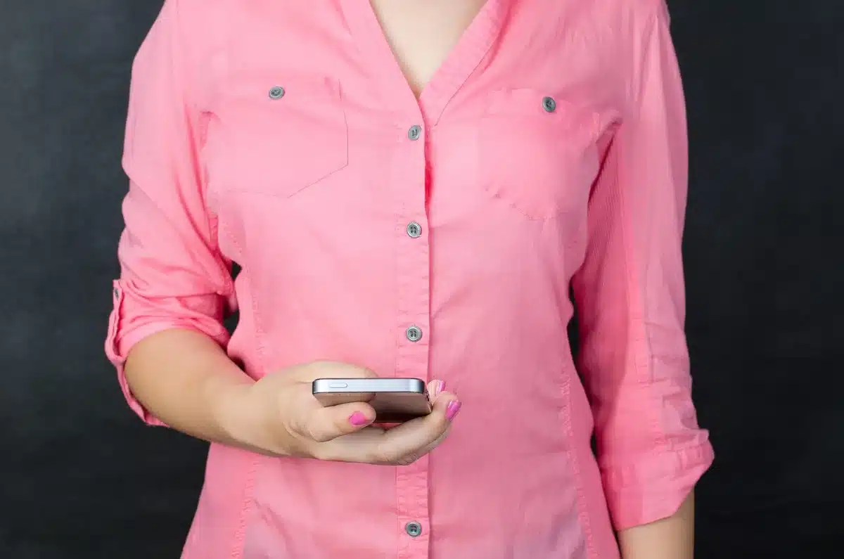 Close-up of an anonymous hand holding an unbranded smartphone, screen dark, against a plain store counter