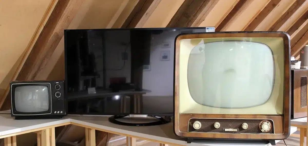 A single unbranded retro television set on a small wooden table showing a paused low-resolution game screen; an anonymous game controller rests beside it, a folded program leaflet nearby