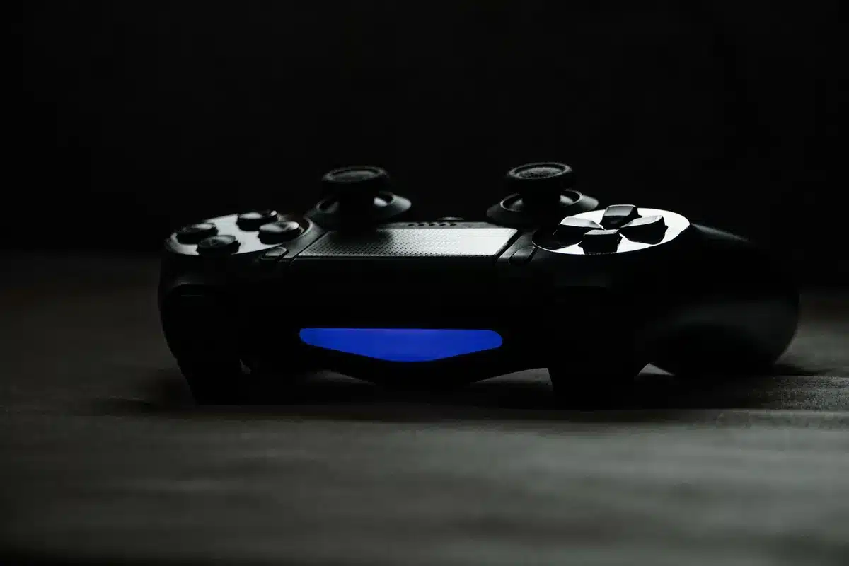 An anonymous close-up of hands holding an unbranded game controller on a tabletop, a blurred vintage TV in the background showing a colorful game screen