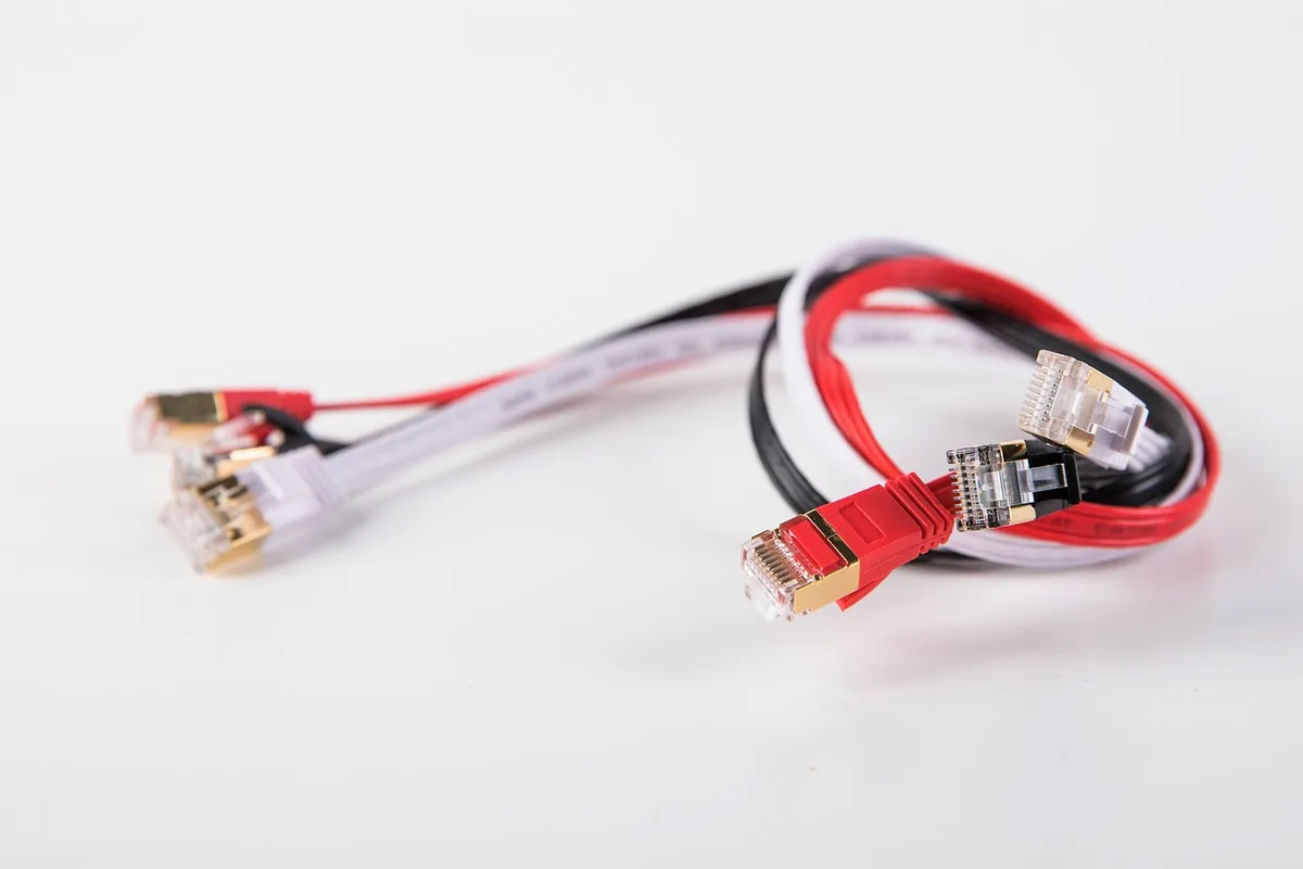 close-up of an unbranded ethernet cable plugged into an adapter on a wooden desk, anonymous hands in background out of focus, no recognizable devices