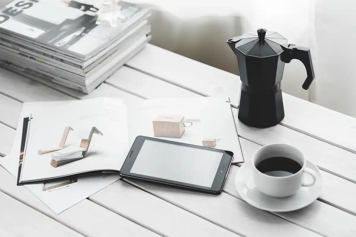 Close-up of an unbranded slim tablet on a table next to a neutral coffee cup, soft indoor light